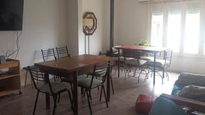 A dining area with a wooden table and chairs, a television mounted on the wall, and a window with curtains.