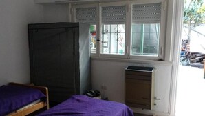 A small room with two beds, a wardrobe, a window with bars, and a door.