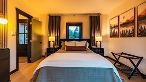 Una habitación de hotel con una cama grande, dos mesitas de noche con lámparas, una ventana con vistas a árboles y una obra de arte en la pared.