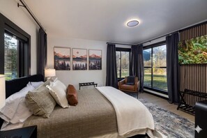 Un dormitorio moderno con una cama grande, un escritorio y una silla. Hay tres cuadros en la pared y una ventana con vistas al exterior.