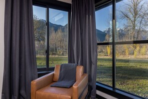 Una habitación con una butaca de cuero y vistas a un campo cubierto de hierba y montañas a través de amplias ventanas.
