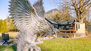 Una escultura de dragón de piedra en un parque, con una cabaña de madera al fondo.