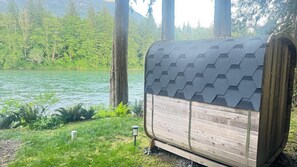 En campingvogn i træ med et sekskantet tag holder ved en sø, omgivet af grøn vegetation og træer.