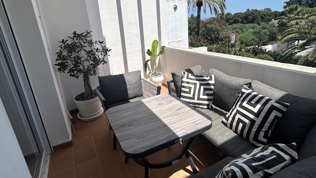 A balcony with a grey sofa, a small table, and a potted plant. - Duplex 'Sotogrande' with Shared Pool, Terrace and Wi-Fi (Sotogrande)