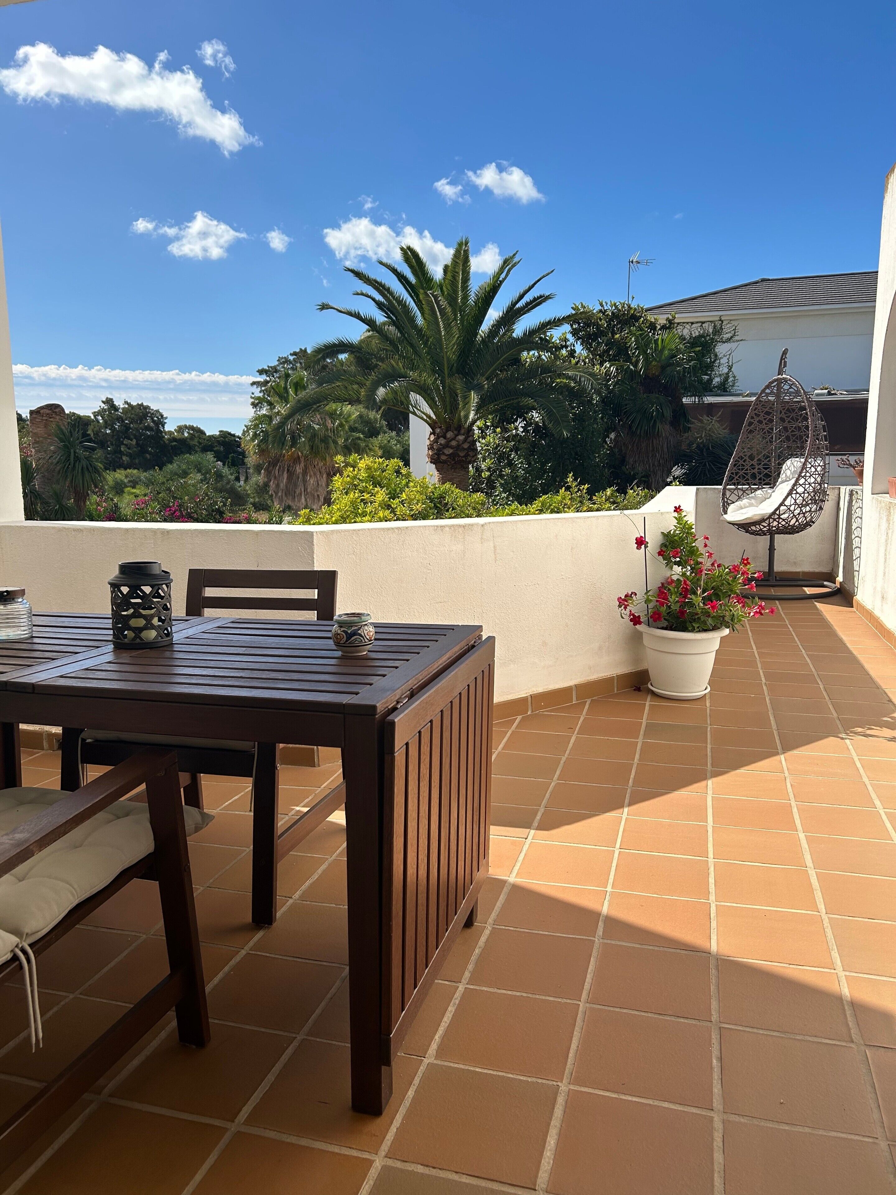 Une terrasse avec une table et des chaises, un fauteuil suspendu et des plantes en pot.