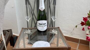 Une table en verre avec une bouteille de CAVA Cabre & Sabate, deux verres et une serviette blanche roulée.
