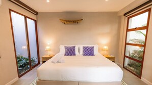 Ein Hotelzimmer mit einem großen Bett, zwei Nachttischlampen, einem Holzschild über dem Bett und Blick auf Grün durch eine Schiebetür.