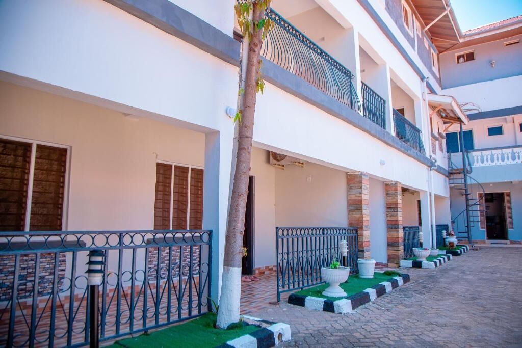 A multi-story hotel with a covered outdoor area, a central staircase, and a row of potted plants along the walkway.