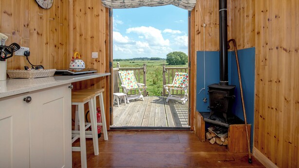 Ein Holzinnenraum mit Küchenbereich, einer Holzterrasse und zwei Stühlen sowie einem Kaminofen.