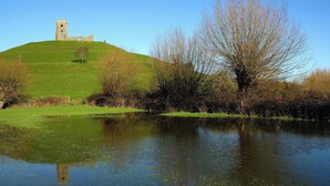 Ein grasbewachsener Hügel mit einem Steinturm und einem sich spiegelnden Gewässer.