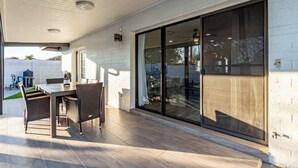 Ein überdachter Patio-Bereich mit Esstisch und Stühlen, einer Glastür zum Verschieben und Blick auf den Garten.