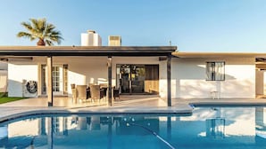 Ein modernes Haus mit Swimmingpool, einer überdachten Terrasse und Gartenmöbeln sowie einer Palme.