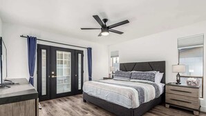 Ein Schlafzimmer mit Bett, Nachttisch, Schreibtisch, Deckenventilator und einer Schiebetür.