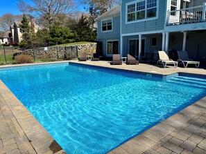Piscina retangular com água azul cristalina, rodeada por um muro de pedra e um deck pavimentado.