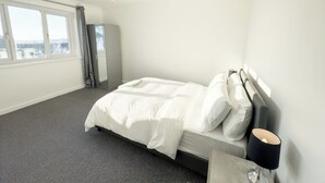 Ein Hotelzimmer mit einem großen Bett, einem Nachttisch mit Lampe, einem Kleiderschrank und Blick auf die Stadt durch das Fenster.