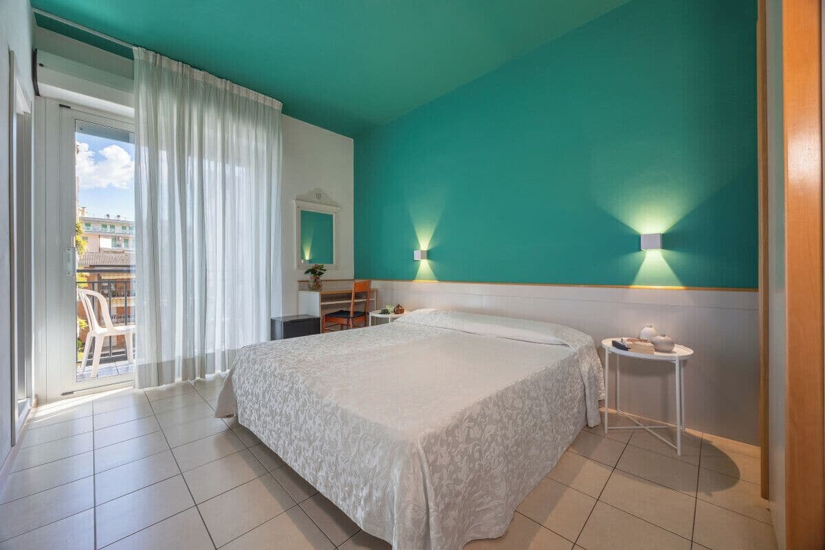 A hotel room with a bed, a small table, a chair, a desk, and a view of the outside.