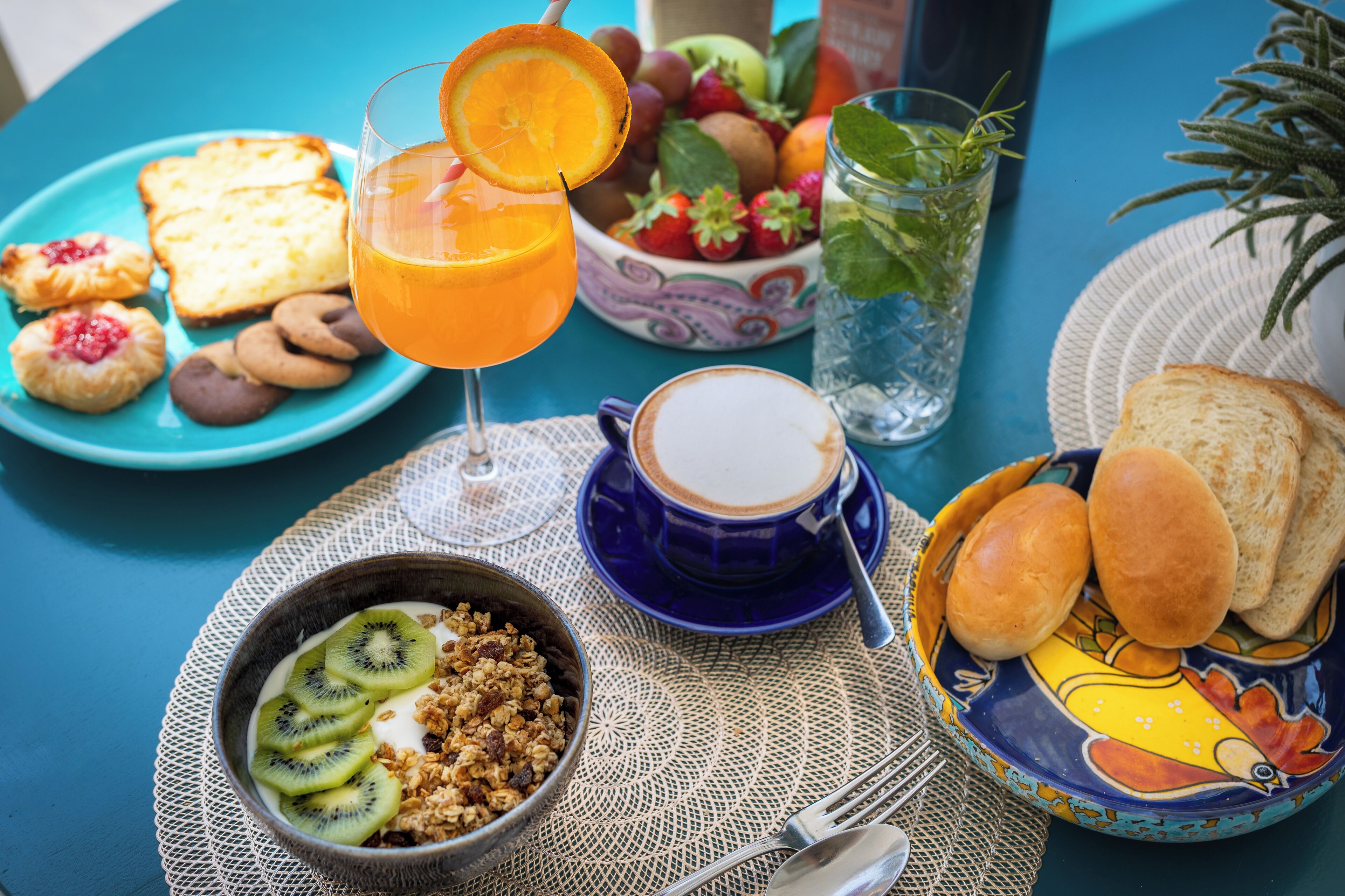 A breakfast table with various food items, a glass of orange juice, a cup of coffee, and a bowl of cereal with kiwi slices.