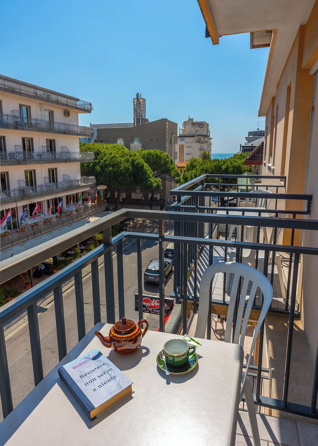 A balcony with a table, a chair, a book, a teapot, and a cup.