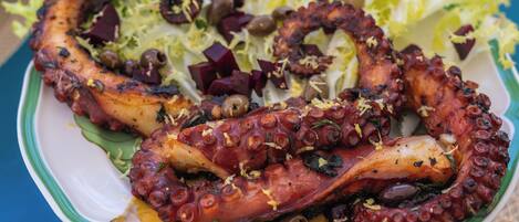 Un plato de pulpo a la parrilla con aceite de oliva, limón y hierbas, acompañado de una ensalada.
