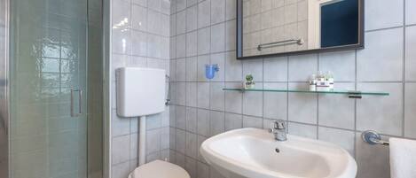 Un bagno moderno con box doccia in vetro, un WC bianco, un lavabo su piedistallo e uno specchio sopra il lavabo.