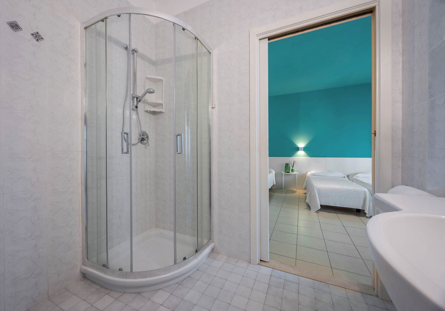 A modern bathroom with a glass-enclosed shower, a white sink, and a teal accent wall.