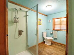 A bathroom with a glass shower enclosure, a toilet, and a window with blinds. - The Old Cow Shed (Eye)