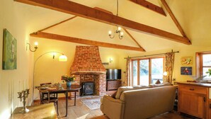 A cozy living room with a fireplace, wooden beams, a sofa, and a dining area with a table and chairs. - The Old Cow Shed (Eye)
