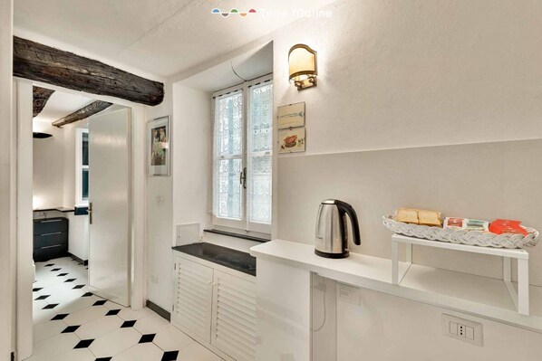 A modern kitchen with a black and white tiled floor, a white countertop, a kettle, and a basket of bread on a shelf. - Harbanella Sea View, Marine Lands (Vernazza)