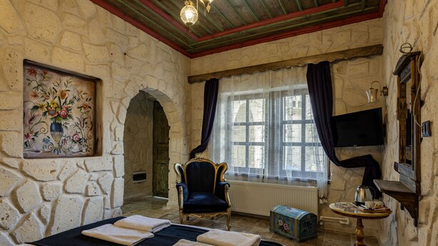 A stone-walled room with a bed, a chair, a table, and a television. - cappadocia keyfiala hotel (Urgup)