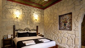 A stone-walled bedroom with a bed, two wall-mounted lights, a nightstand, and a decorative painting. - cappadocia keyfiala hotel (Urgup)