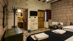 A rustic room with a bed, a television, a coat rack, and a wooden door. - cappadocia keyfiala hotel (Urgup)