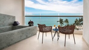 A balcony with a view of the ocean, two wicker chairs, a small table, and a concrete bench. - Ocean View in a Beach Front Resort and Spa.  (Incl. All-Inclusive for 2 Adults) (Puerto Vallarta)