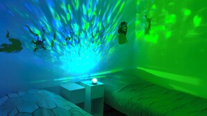 A room with two beds, a nightstand, and a wall with a green light projection. - House with courtyard, 3-minute walk from the beach 🏖️ - the sea breeze 🌊 (Gravelines)