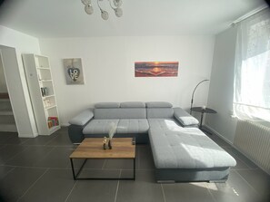 A modern living room with a grey sectional sofa, a wooden coffee table, a bookshelf, a painting, and a floor lamp. - House with courtyard, 3-minute walk from the beach 🏖️ - the sea breeze 🌊 (Gravelines)