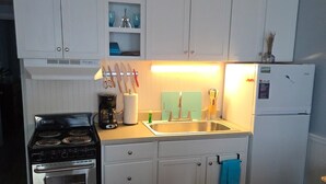 A compact kitchen with white cabinets, a stove, a sink, and a refrigerator.
