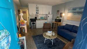 A compact living space with a kitchenette, a blue sofa, a coffee table, and a dining area.