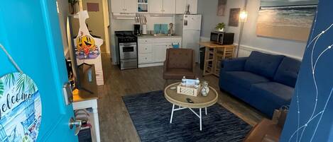 A compact living space with a kitchenette, a blue sofa, a coffee table, and a dining area.