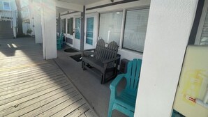 A covered outdoor seating area with wooden flooring, a bench, and two turquoise chairs.
