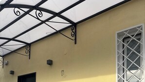Un bâtiment doté d’un mur en pierre, d’une porte noire, d’une fenêtre à motifs géométriques et d’un patio couvert.