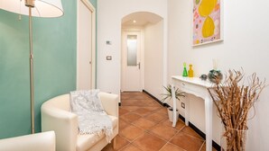 Ein Flur mit einem weißen Stuhl, einer Stehlampe, einem weißen Beistelltisch mit Dekorationen und einem farbenfrohen abstrakten Gemälde an der Wand.