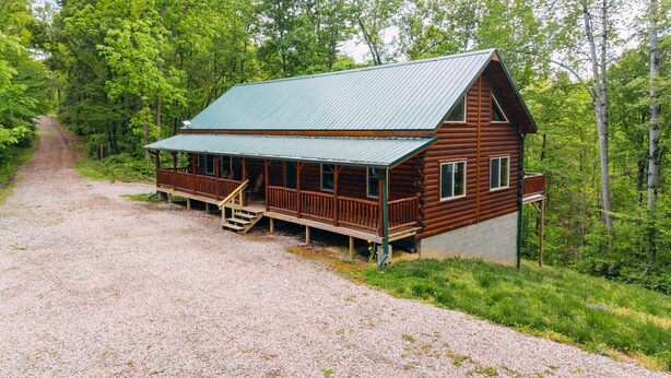 En træhytte med veranda, grusvej og skov i baggrunden.