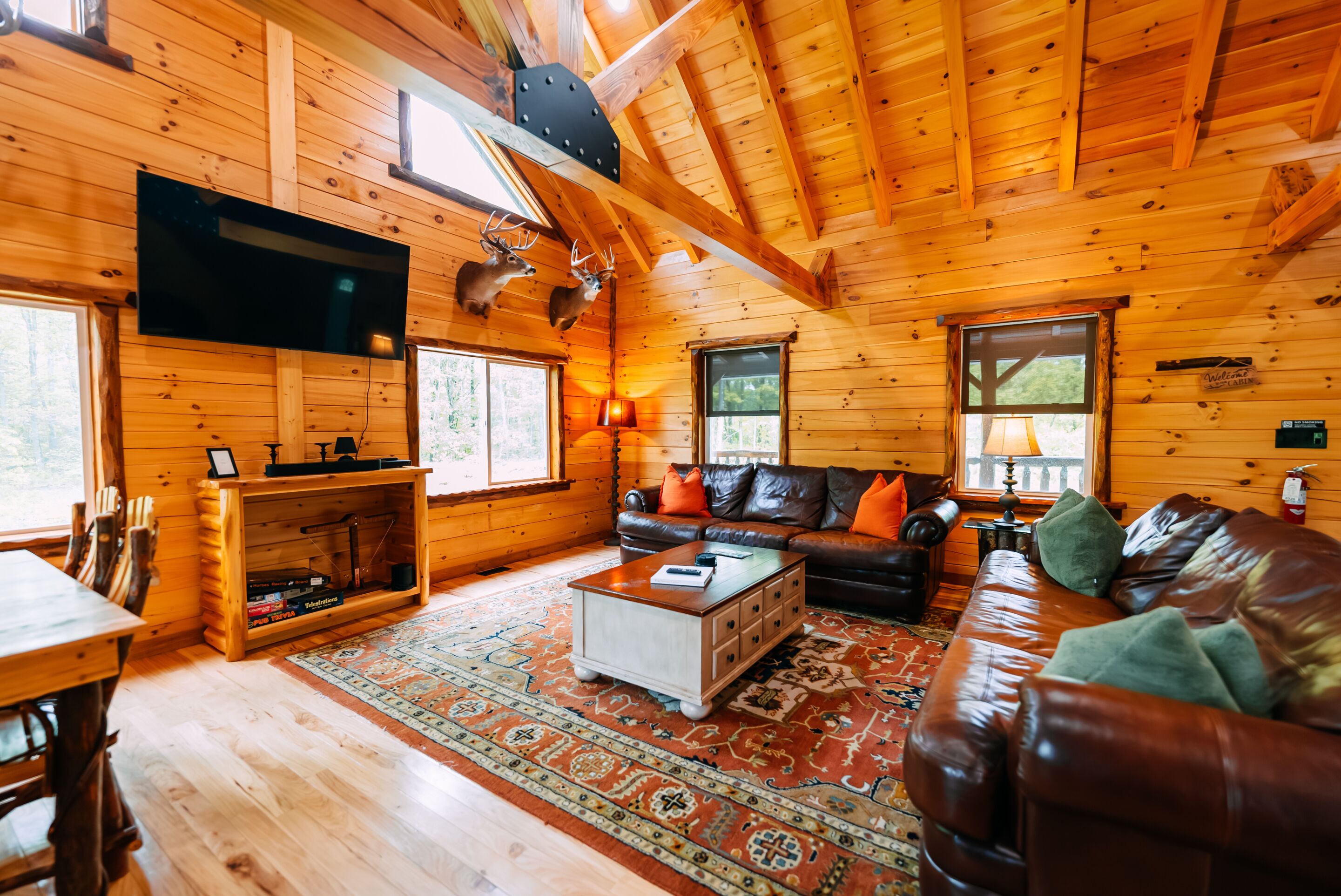 Ein Blockhaus-Interieur mit Holzbalkendecke, einer Ledersofa, einem Fernseher und einem Kamin.