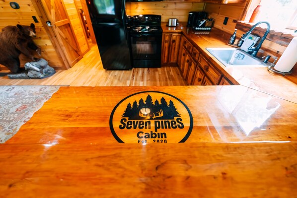 Een houten cabin interieur met het logo 'Seven Pines Cabin' op het aanrecht, een koelkast, fornuis en houten kastjes.