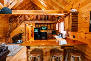L’intérieur d’une cabane en rondins, avec un escalier en bois, un coin cuisine et un bar avec des tabourets.