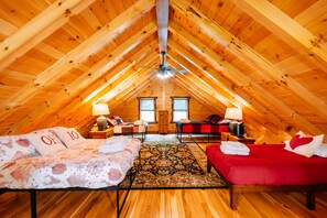 Un dormitorio en el ático con vigas de madera, dos camas, un sofá rojo, una alfombra y un ventilador de techo.