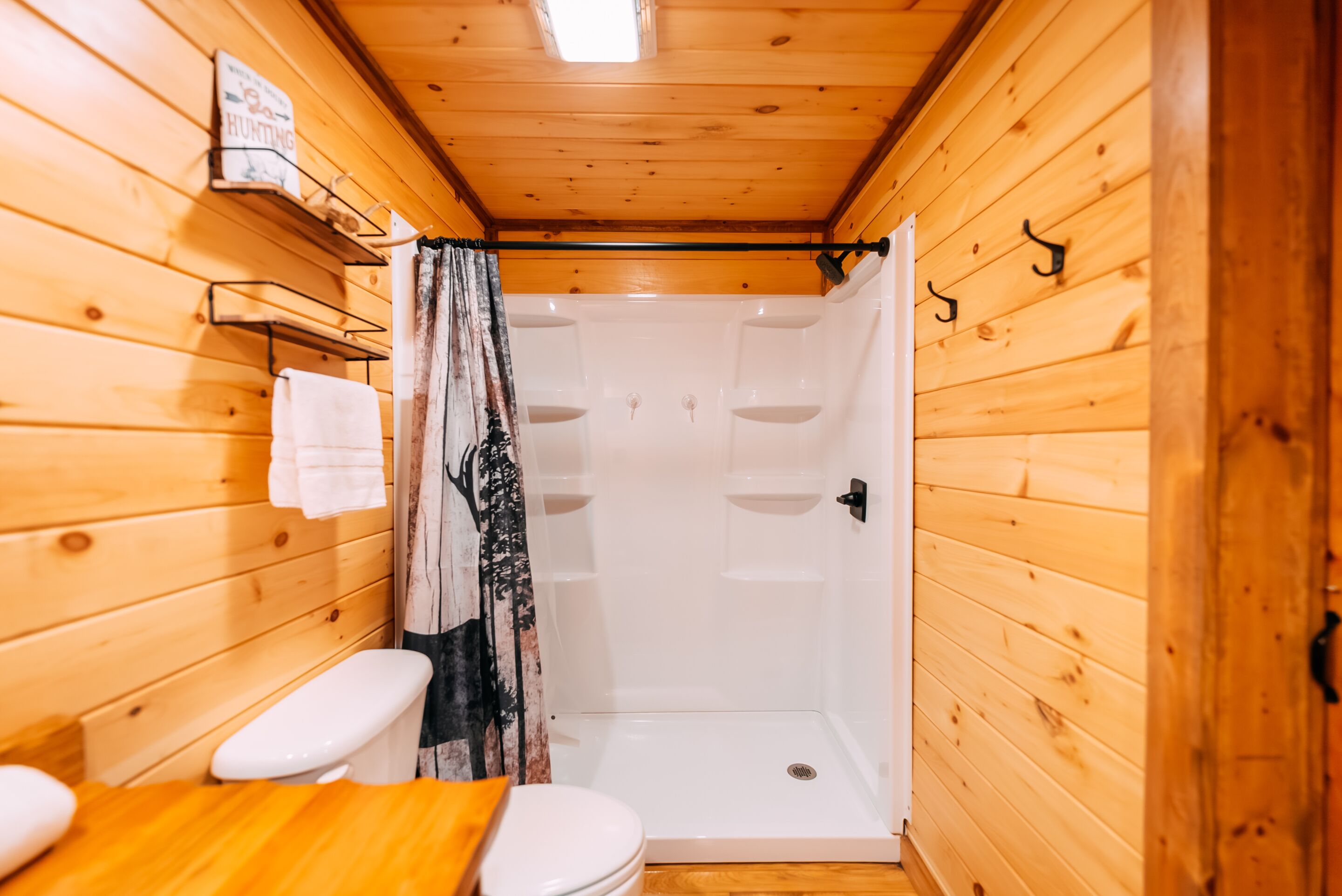 A wooden cabin bathroom with a shower, toilet, and a towel rack.