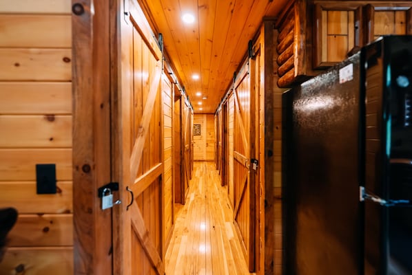 Un pasillo de madera con puertas a ambos lados, un refrigerador a la derecha y un cartel en la pared.