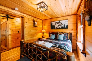 Een houten blokhut van binnen met een bed, een lamp, een bordje met de tekst 'Cabin Life' en een decoratie van een hertenkop.