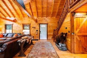 Een houten cabin met een bank, een vloerkleed, een beerbeeld en een deur.