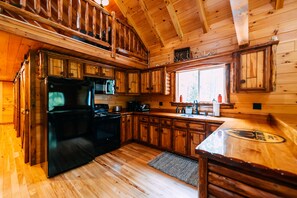 Une cuisine de style rustique, avec des murs en bois, un réfrigérateur noir et une fenêtre donnant sur les arbres.
